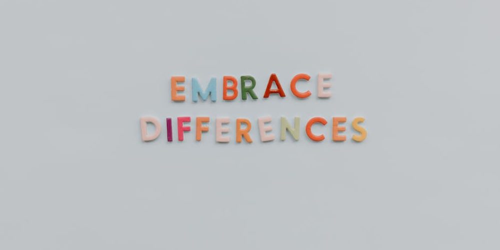 Colorful letters spelling 'Embrace Differences' on a minimalist gray background highlighting inclusivity and diversity.